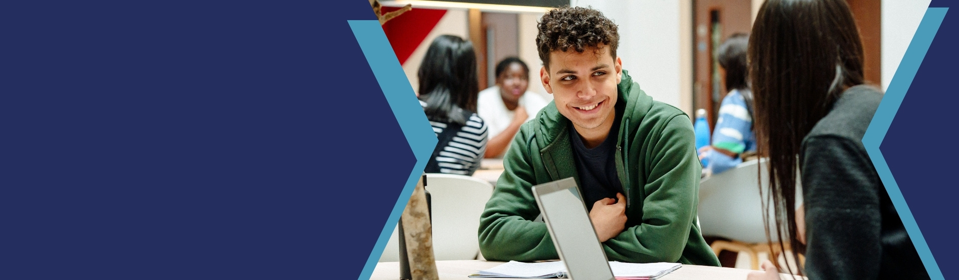 Young man smiling at another person working on a laptop