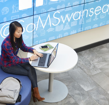 Student working on a laptop at a table in Swansea University School of Management