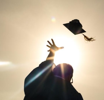 student in graduation gown throwing cap in the air