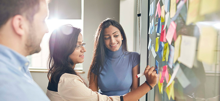 Two females writing on post-it notes stuck on a wall