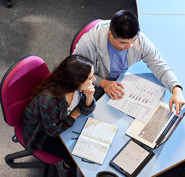 A male and female student sitting at desk with notes and laptop