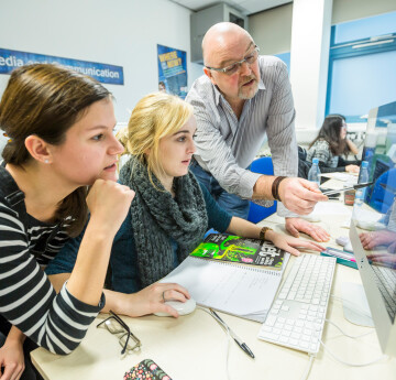 Tutor assisting two students in a CAD lab. The tutor is pointing at a computer screen.