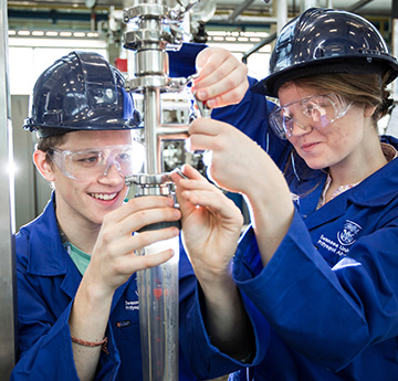 Two people wearing overalls, glasses and hard hats