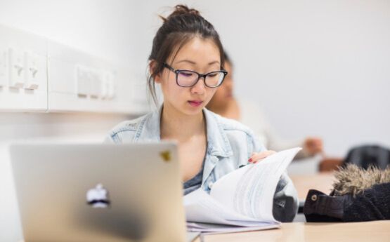 Student in the library. She is using her laptop.